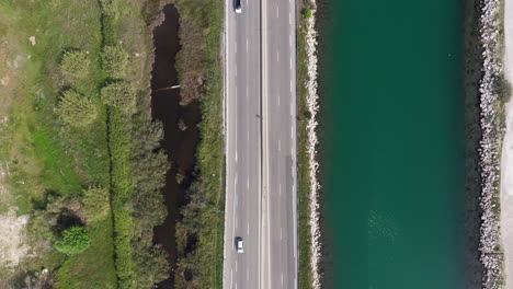 Road-along-a-canal-aerial-top-down-shot-with-cars